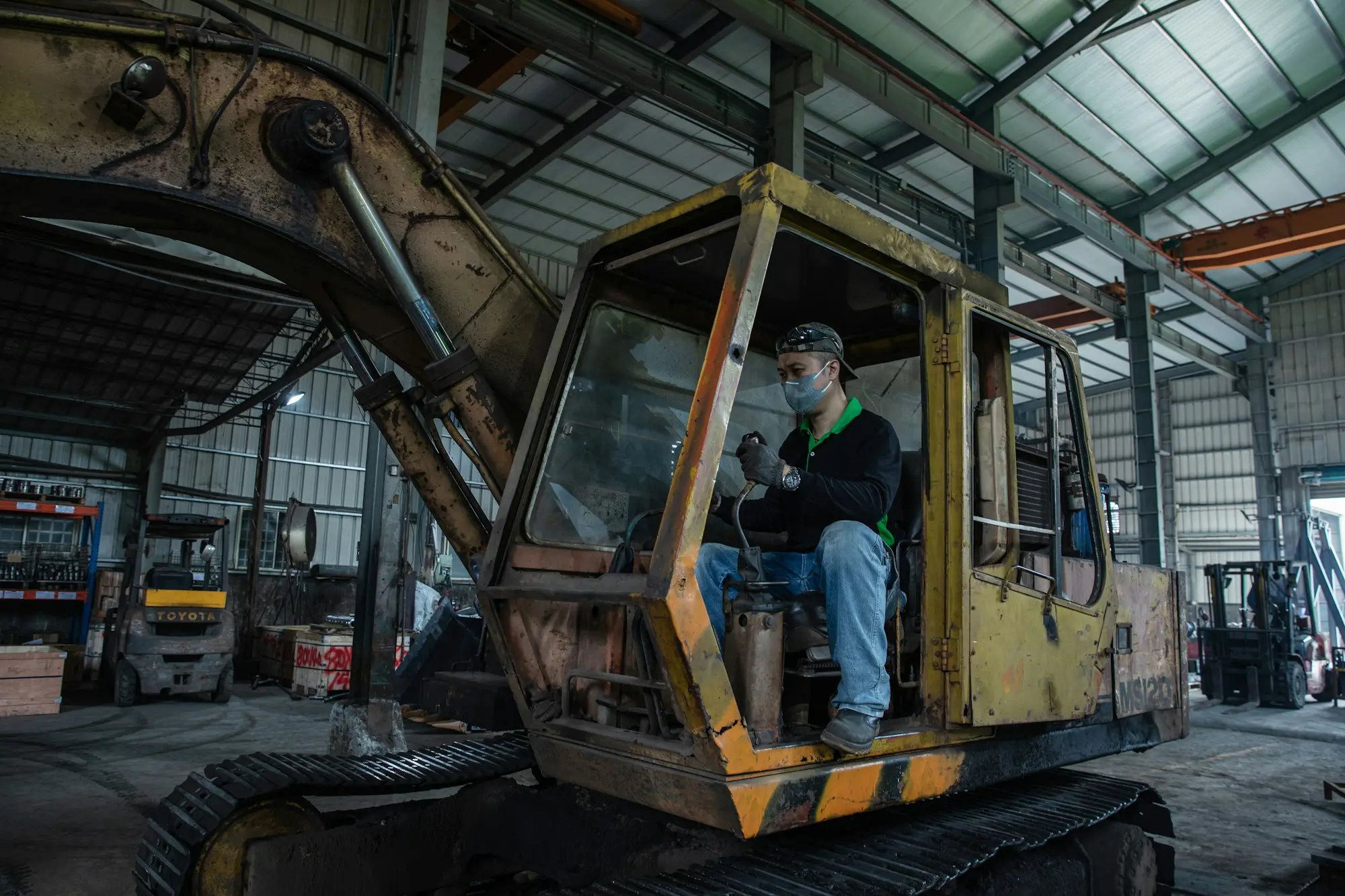 Operator inside a broken-down excavator in a repair shed